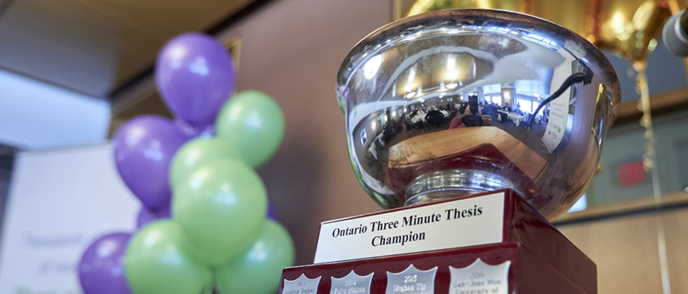 The 3MT trophy on a table with a bunch of balloons behind.