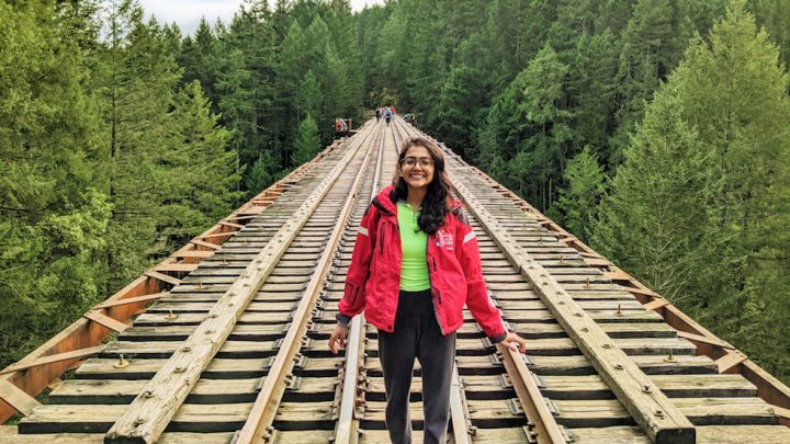 Global Health alum Himani Bhatnagar stands on a train bridge with tree tops lining each side.