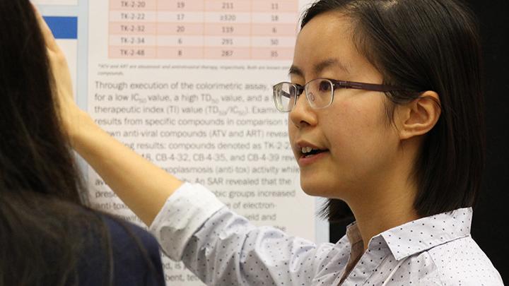 An undergraduate student points to her poster as she speaks to an attendee at a past USRA Poster Session