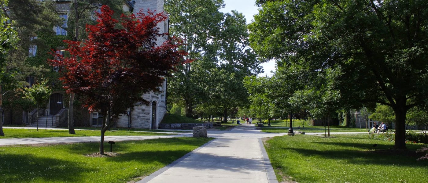 Students walk through the centre of McMaster's main campus during Spring, as trees are in full bloom.