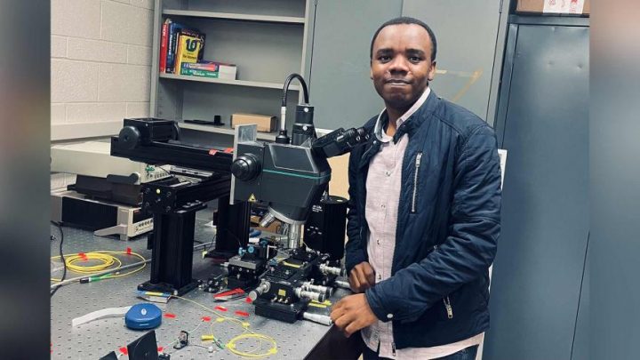 Hamidu Mbonde stands beside a large machine in a lab in Engineering.