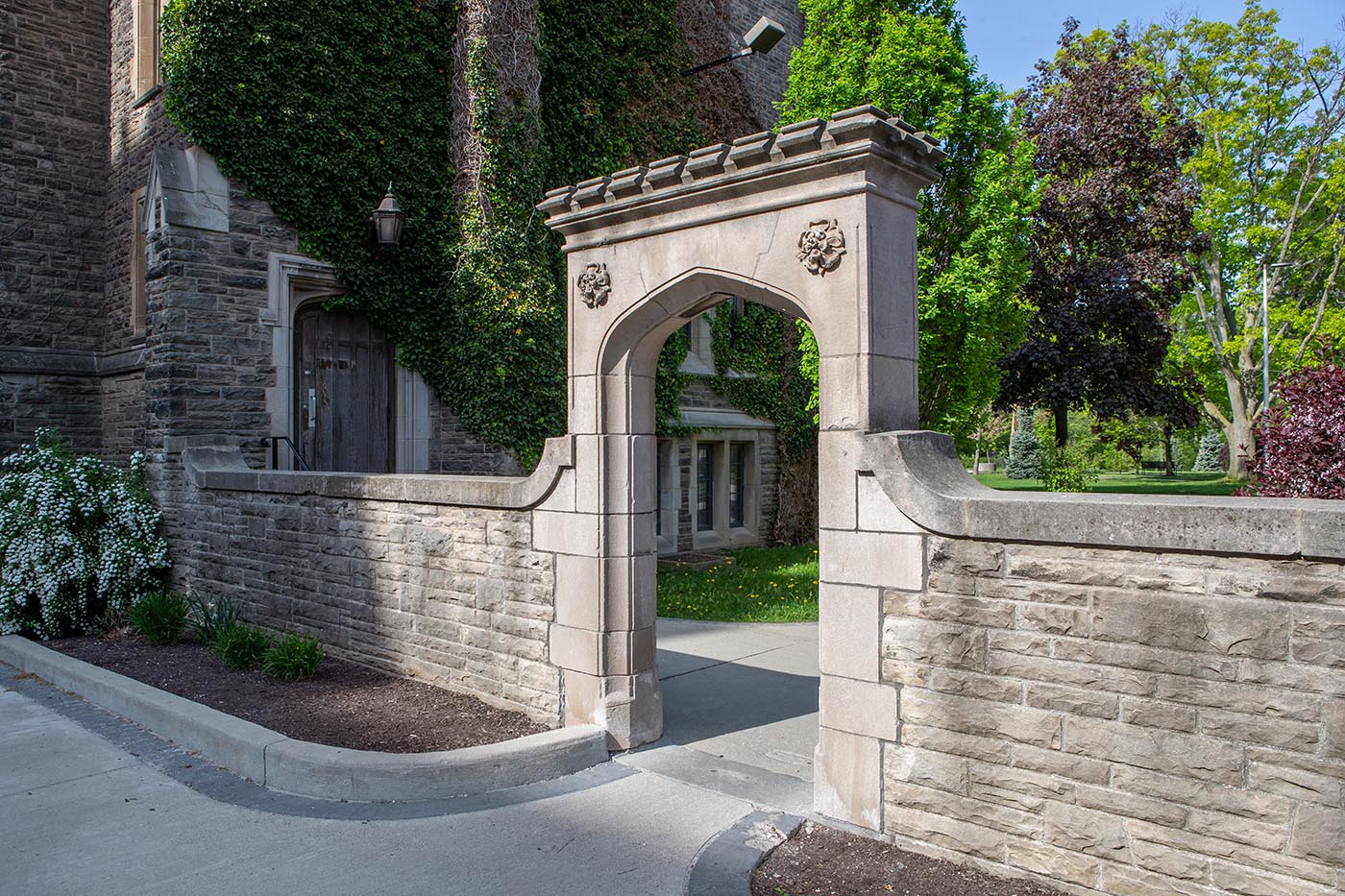 The sun shines on a stone archway in front of an old stone building on McMaster's campus.